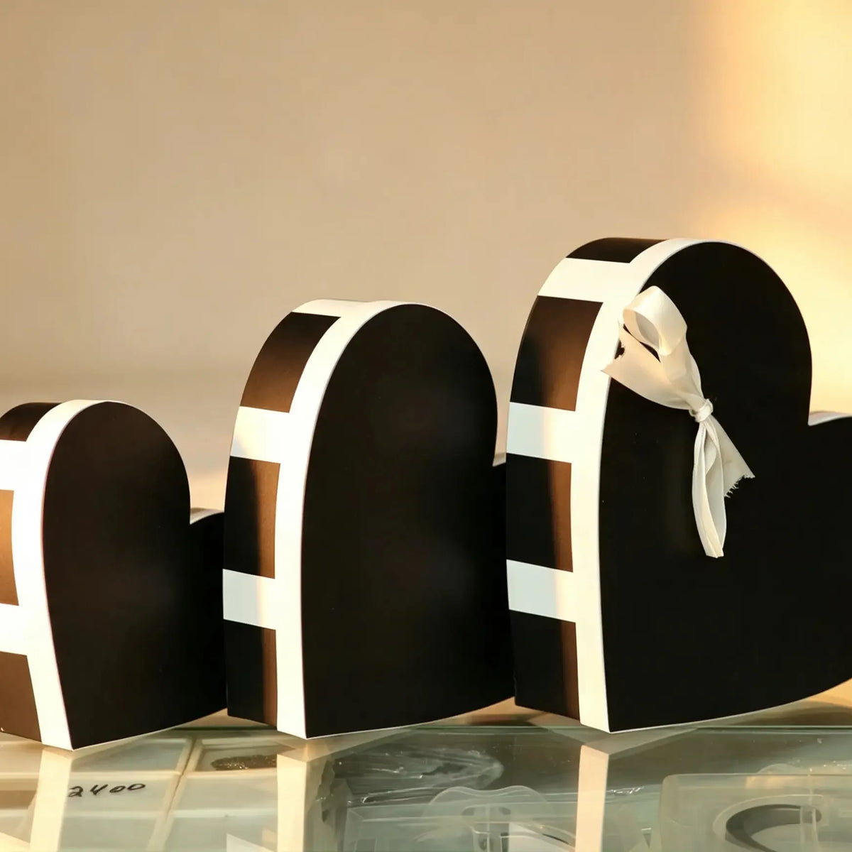 Nested set of three black heart-shaped gift boxes with a white trim band and cream ribbon bow on the largest box