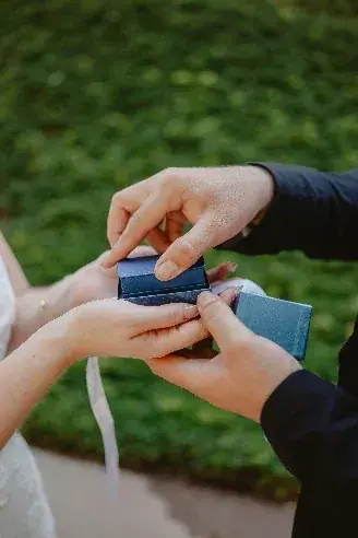 A small leatherette ring box opened between two pairs of hands.