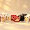Full lineup of nested gift boxes in pink, beige, off-white, red, and black, each with a clear window