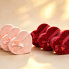 Three graduated pink heart-shaped velvet gift boxes with satin bows beside red velvet heart boxes