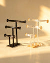 Two three-tier T-bar bangle stands side by side, one black metal and one clear acrylic with gold-tone caps