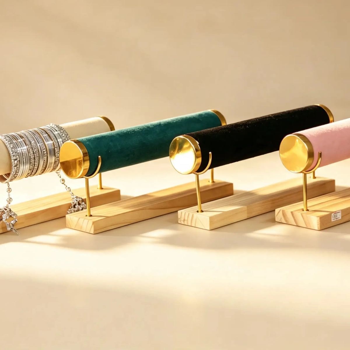 Four velvet-topped bangle stands in cream, teal, black, and pink, one holding stacked bracelets, on wood bases.