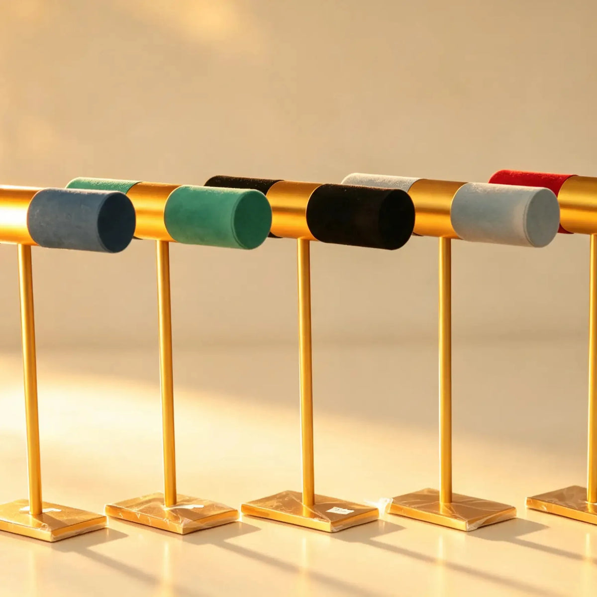Five bangle stands with navy, green, black, grey, and red velvet bars on gold-tone poles with marble-look bases