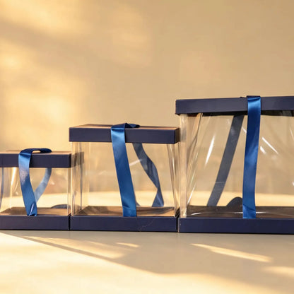 Three navy blue-trimmed clear PVC cake boxes nested together with satin ribbon ties