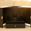 Black gift box with doors open, revealing a heart-shaped display and a drawer with a gold-tone knob