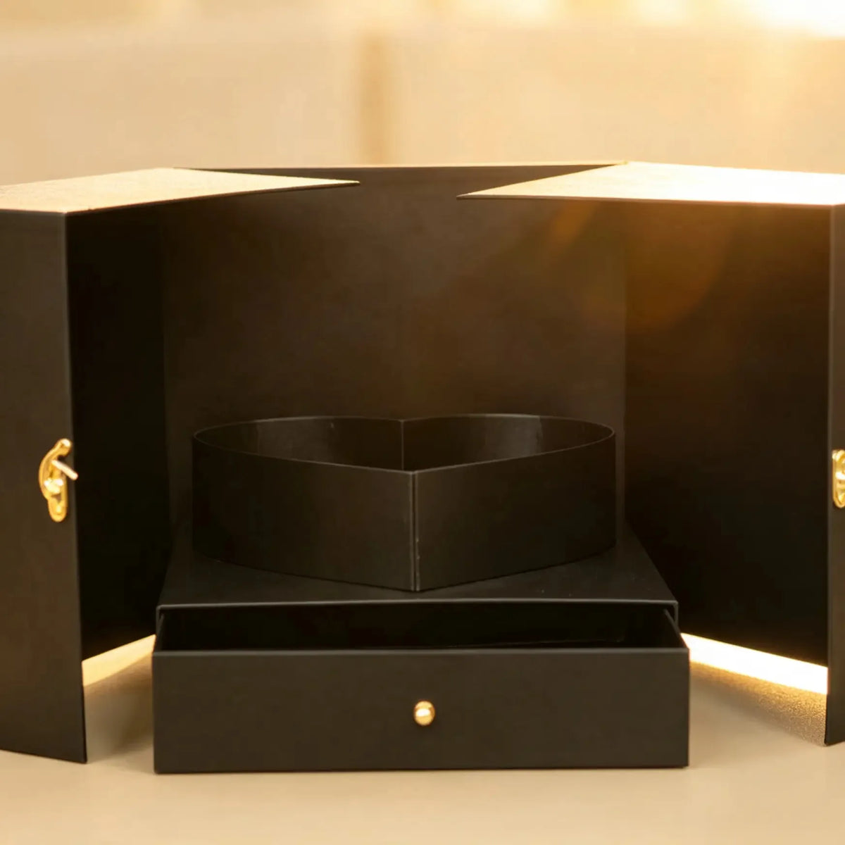 Black gift box with doors open, revealing a heart-shaped display and a drawer with a gold-tone knob