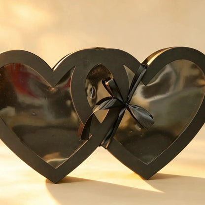 Black double-heart shaped gift box with clear window panels and a black ribbon bow
