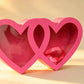 Pink double-heart shaped gift box with clear window panels and a pink ribbon inside