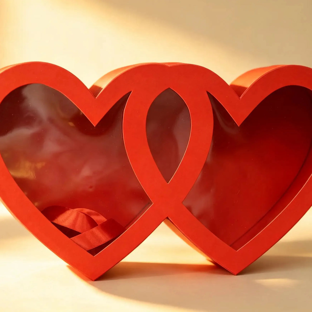 Red double-heart shaped gift box with clear window panels and a red ribbon inside