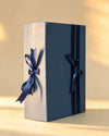 Navy blue folding gift box with cream side panel and two navy ribbon bows