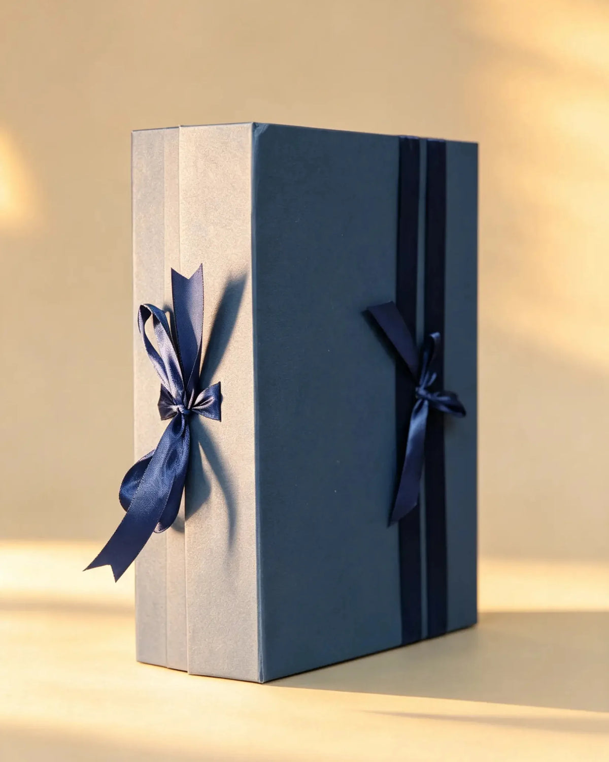 Navy blue folding gift box with cream side panel and two navy ribbon bows