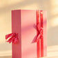 Pink folding gift box with two coral-pink ribbon bows down the front