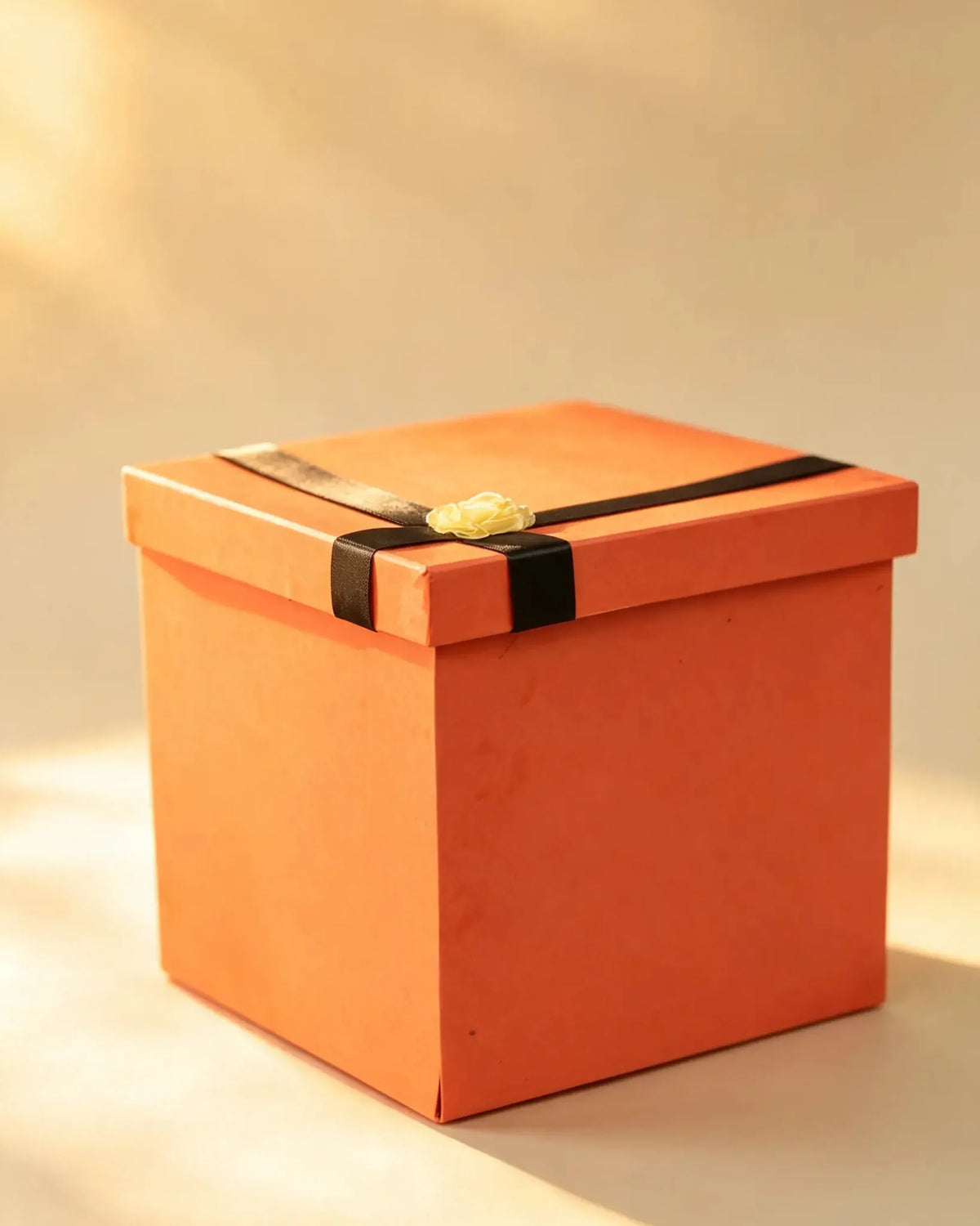 Square gift box in a warm rust tone with a black ribbon bow and small flower accent