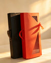 Black and red tall gift boxes with leather handles and ribbon-tied window fronts, standing side by side