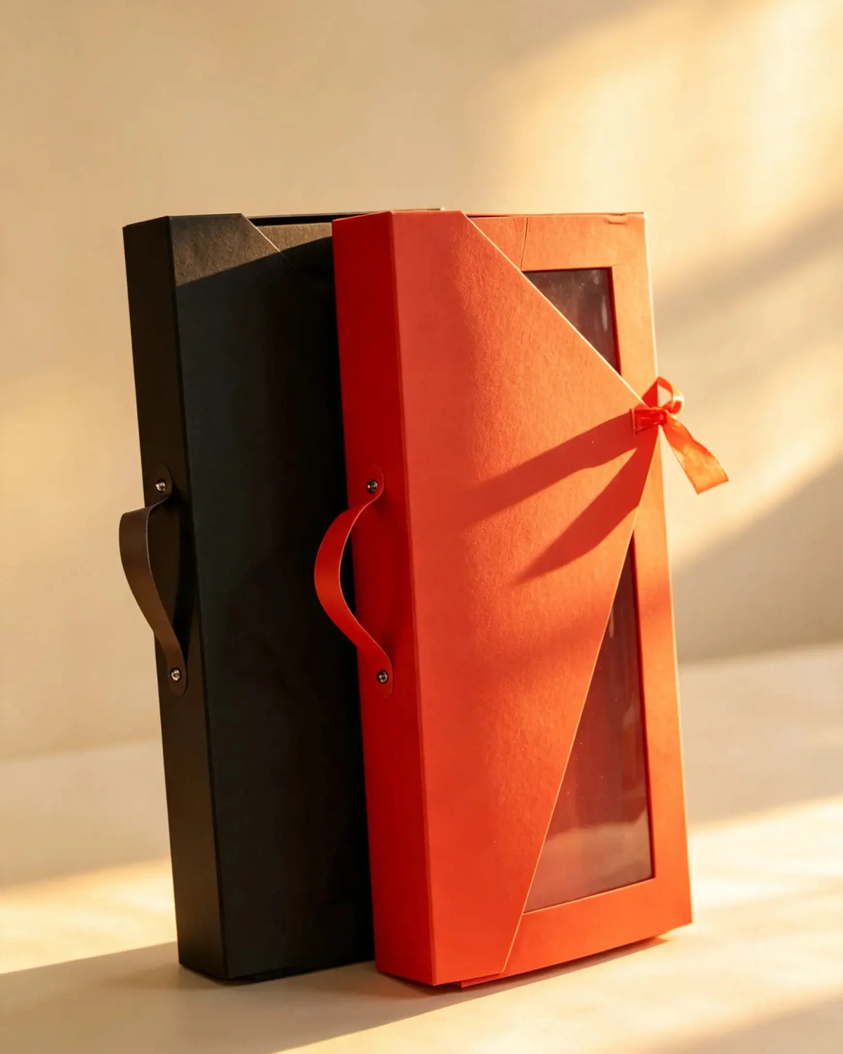 Black and red tall gift boxes with leather handles and ribbon-tied window fronts, standing side by side