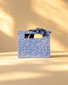 Blue gift bag with white floral vine print and a navy ribbon bow handle