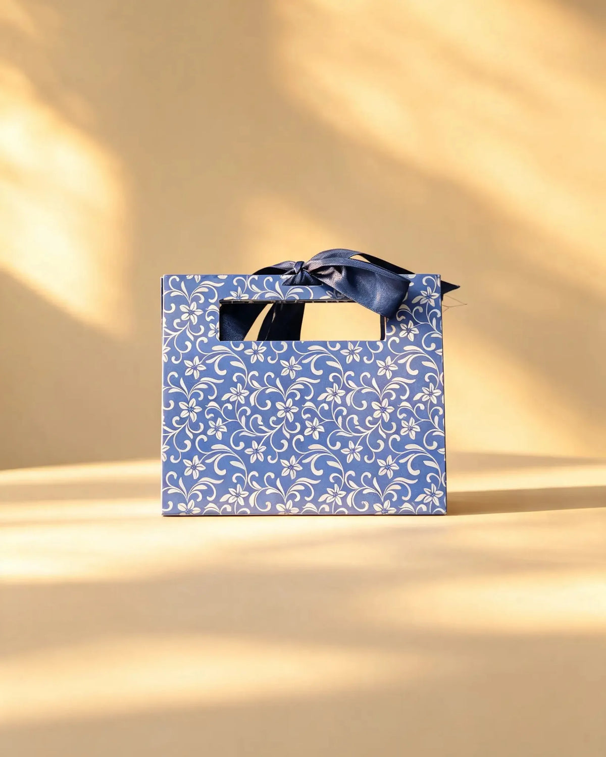 Blue gift bag with white floral vine print and a navy ribbon bow handle