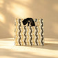 Gold and black wave-striped gift bag with a black ribbon bow handle