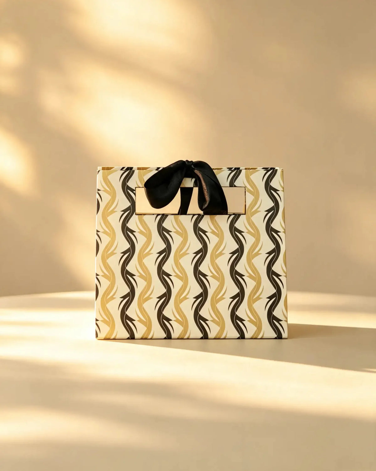 Gold and black wave-striped gift bag with a black ribbon bow handle