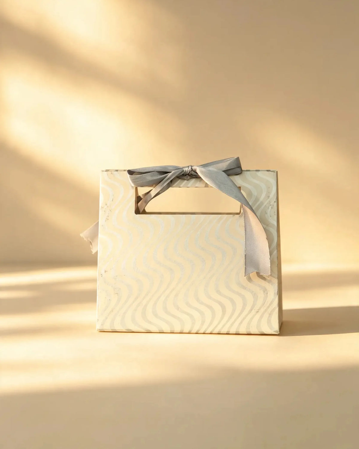 Ivory gift bag with a subtle tonal wave pattern and a grey ribbon bow handle