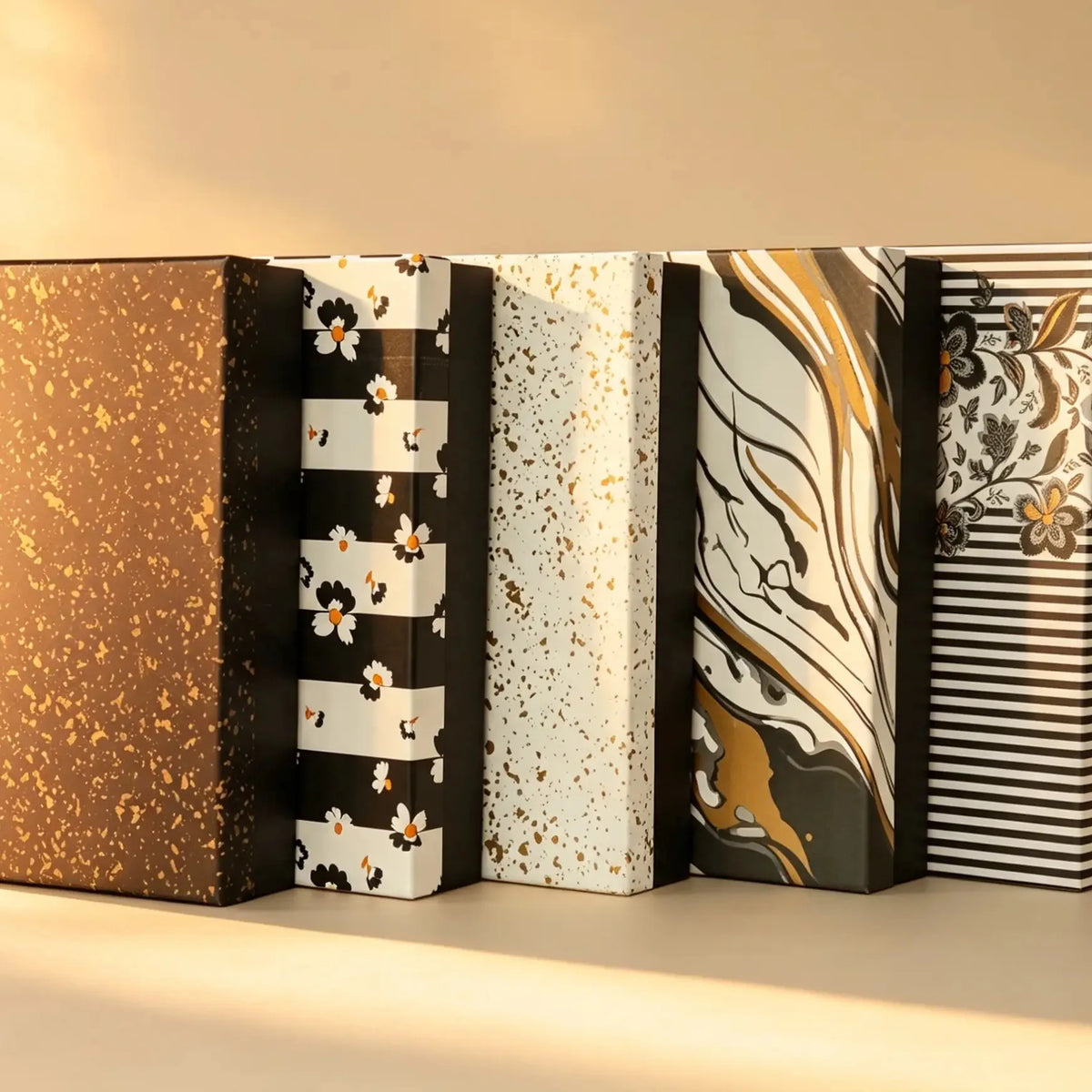 Row of five gift boxes in speckled, floral, and marbled foil-print patterns