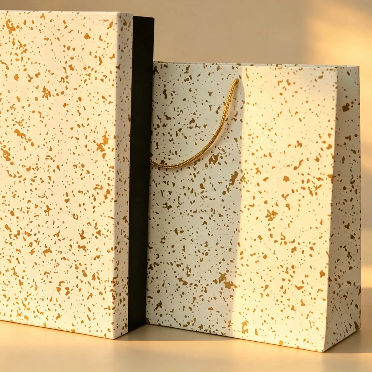 Cream gift box with gold speckle print beside a matching speckled carry bag