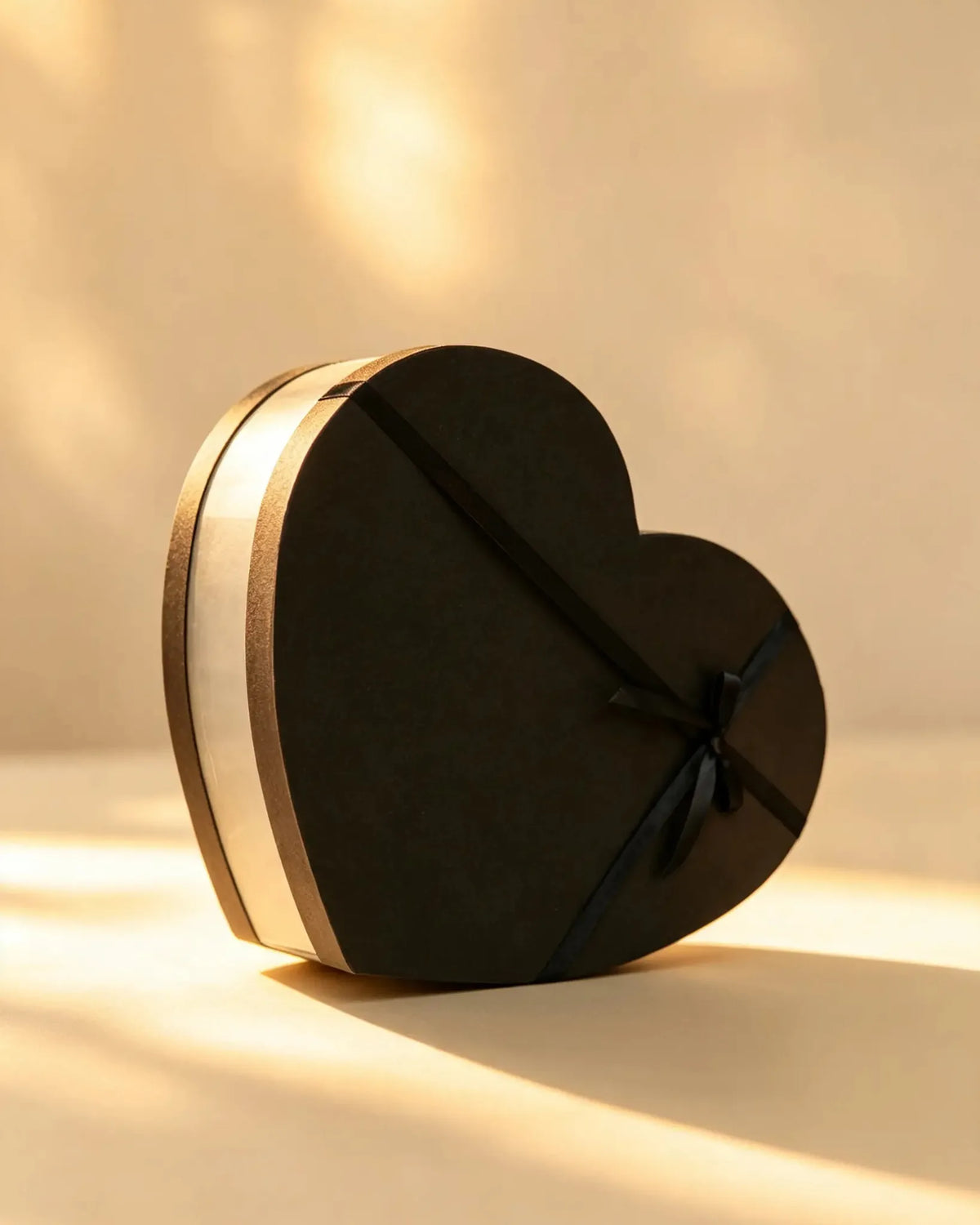 Black heart-shaped gift box with a gold trim band and black ribbon bow