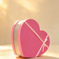 Pink heart-shaped gift box with a gold trim band and pink ribbon bow