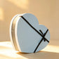 Sky blue heart-shaped gift box with a gold trim band and black ribbon bow
