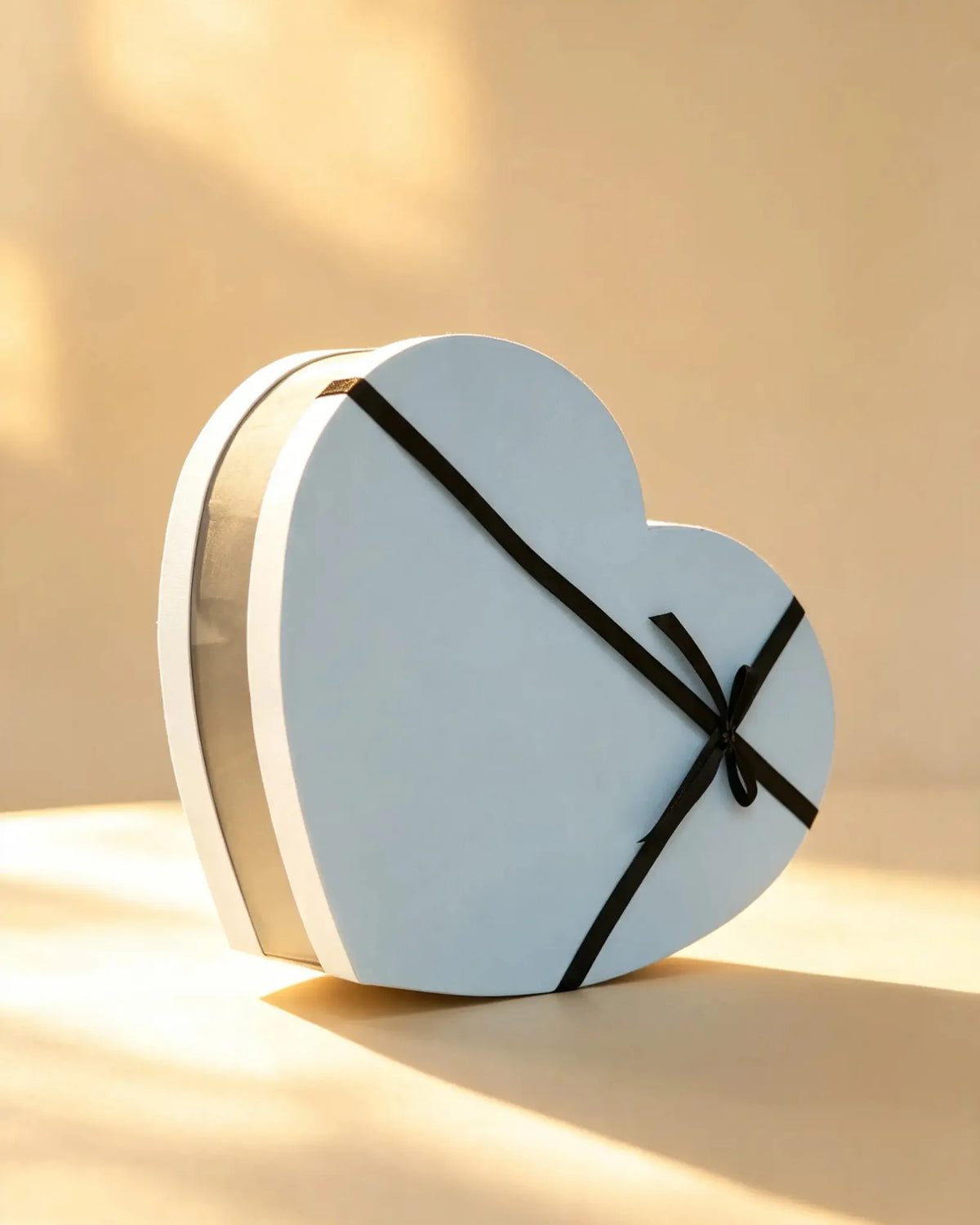 Sky blue heart-shaped gift box with a gold trim band and black ribbon bow