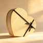 Cream heart-shaped gift box with a gold trim band and black ribbon bow