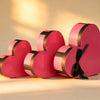 Nested set of three pink heart-shaped gift boxes with a gold trim band and black ribbon bow on the largest box