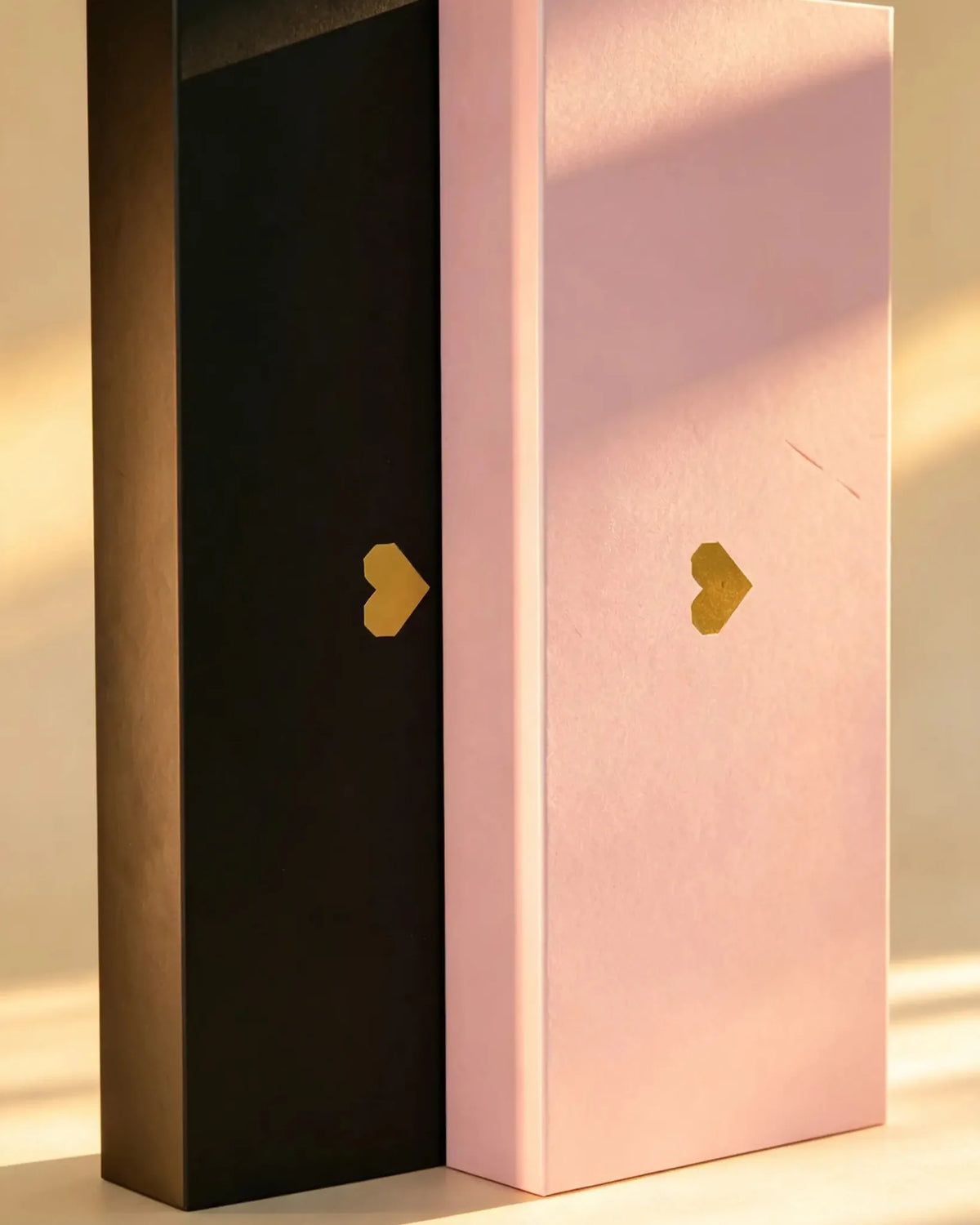 Black and pink LOVE gift boxes standing side by side, each with a small gold foil heart