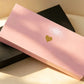 Closed pink gift box with a gold foil heart, leaning against a black box