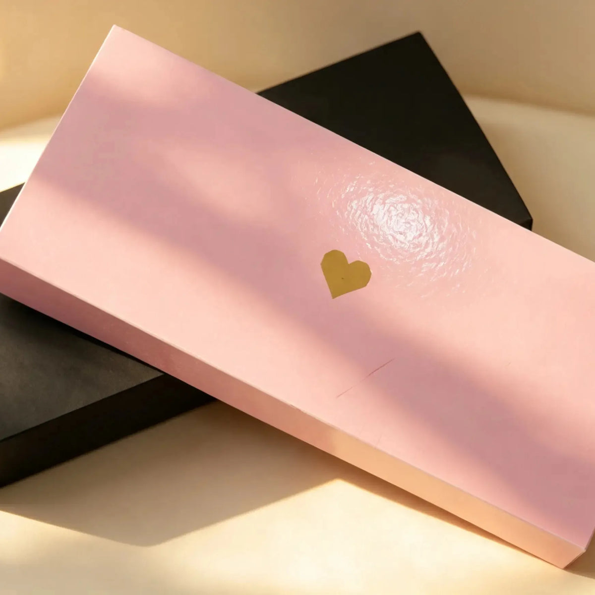 Closed pink gift box with a gold foil heart, leaning against a black box