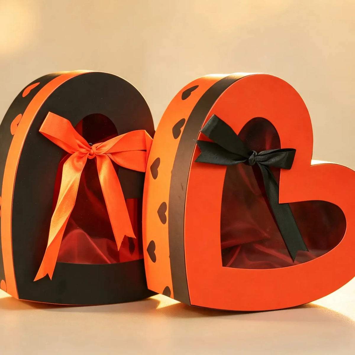 Two heart-shaped window gift boxes with ribbon bows, one black with orange trim and one orange with black trim