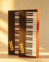 Two piano key-patterned gift boxes with gold LOVE lettering shown side by side