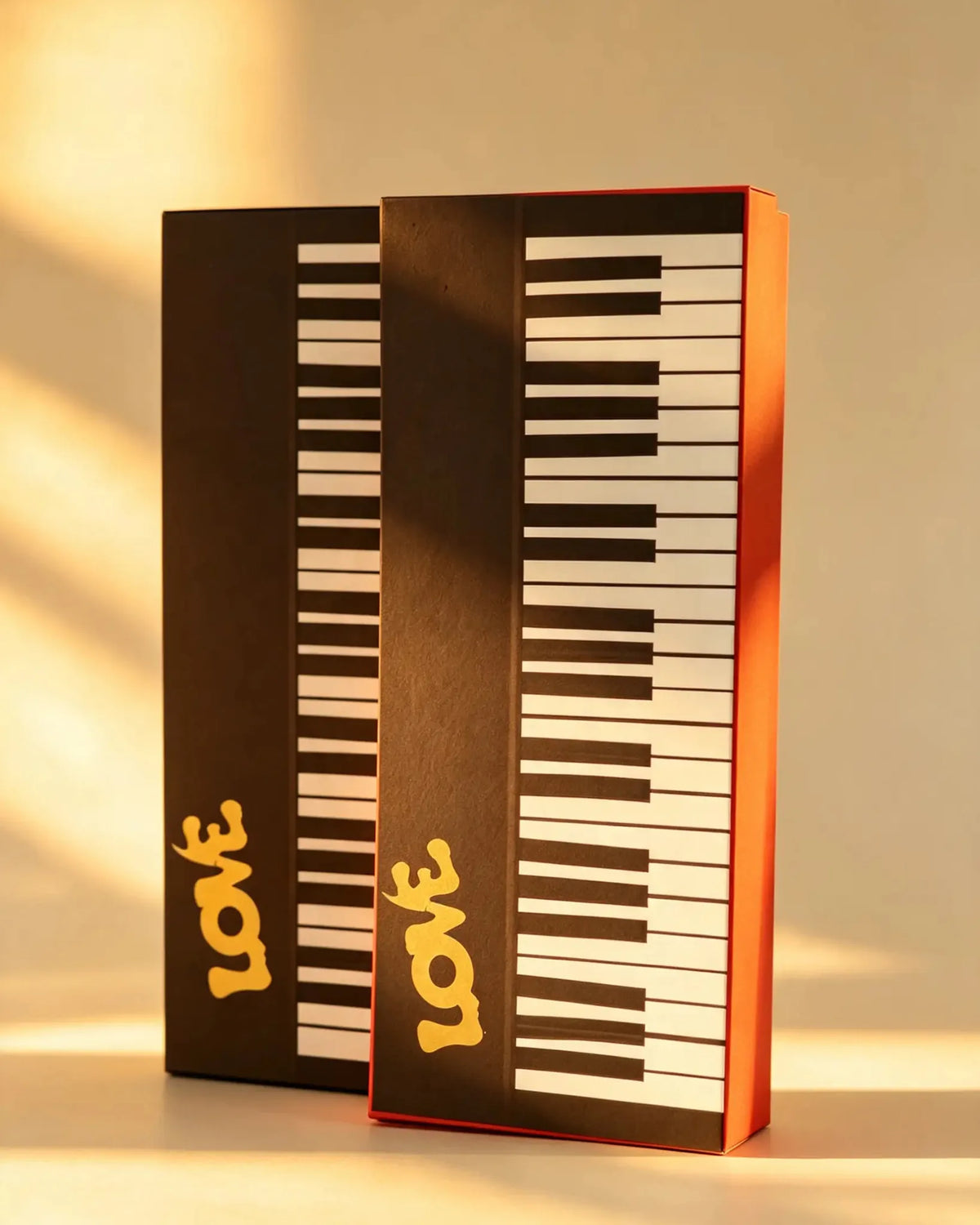 Two piano key-patterned gift boxes with gold LOVE lettering shown side by side