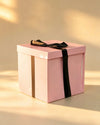 Pink gift box with black ribbon bow and gold stripe accent, closed