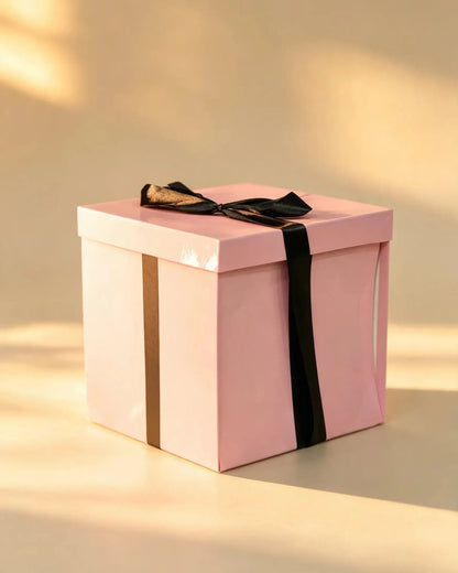 Pink gift box with black ribbon bow and gold stripe accent, closed
