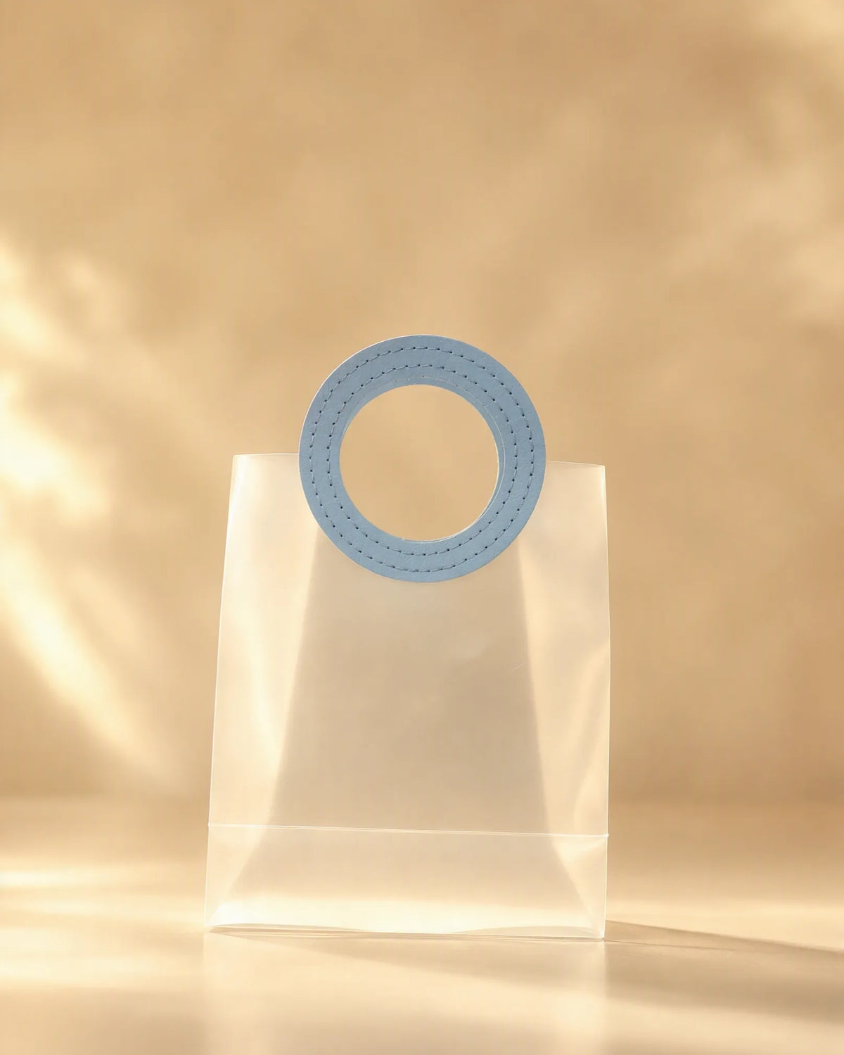 Clear PVC gift bag with round blue handle against warm backdrop