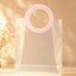 Clear PVC gift bag with pink round handle against dried floral background