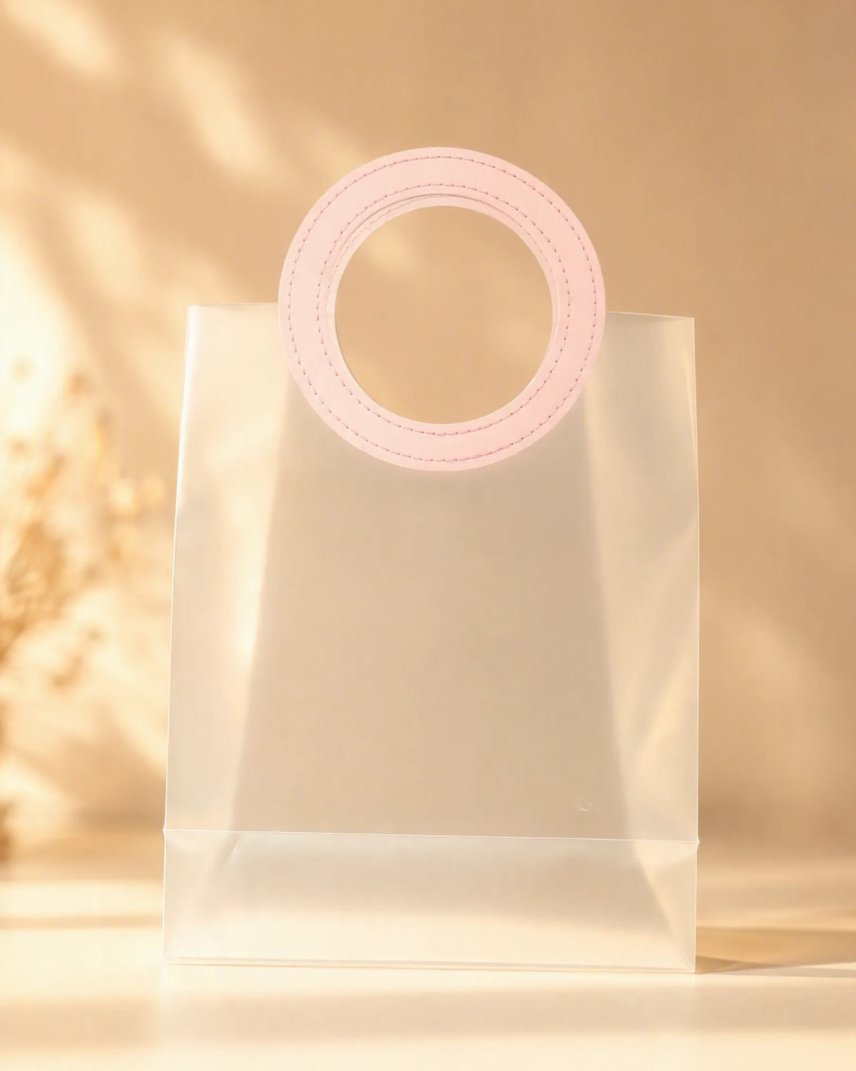 Clear PVC gift bag with pink round handle against dried floral background