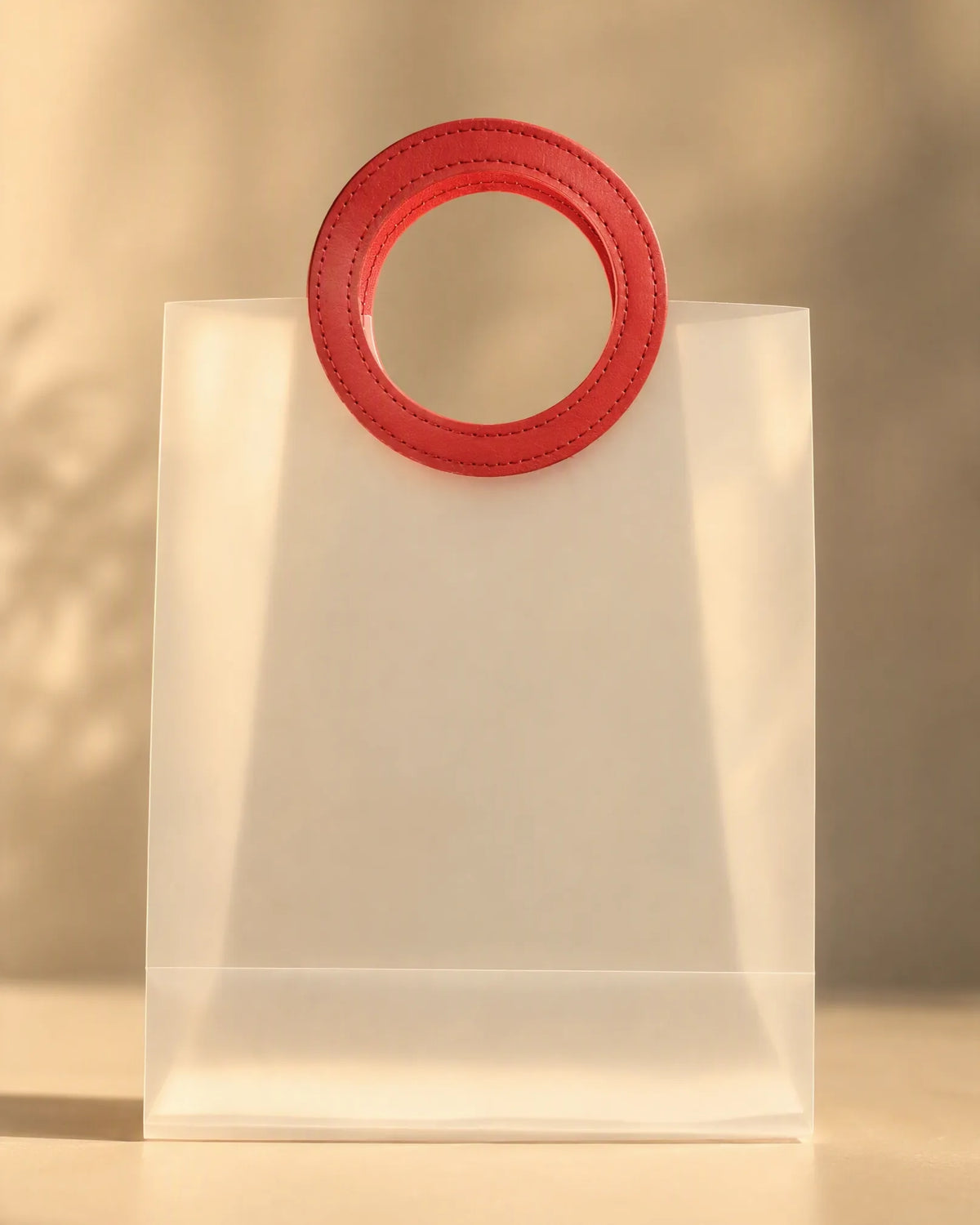 Detail close-up of the stitched red round handle on a clear PVC gift bag