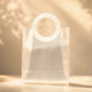 Frosted white PVC gift bag with round handle, front view with leaf shadow