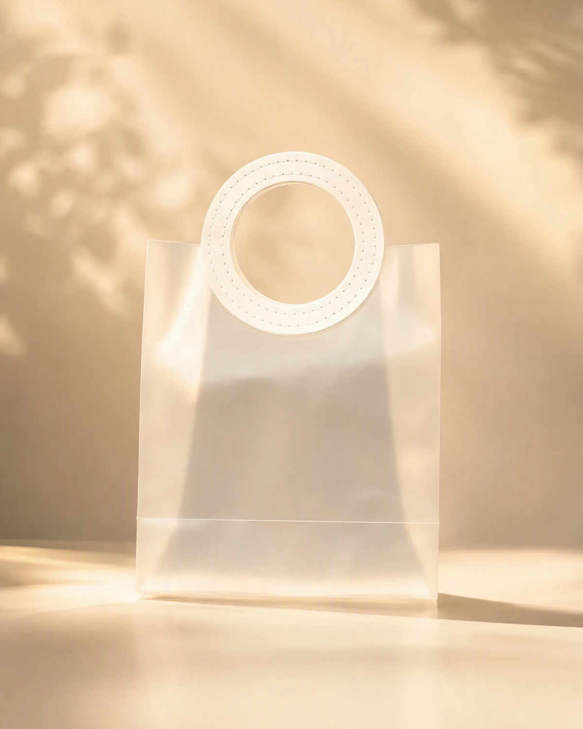 Frosted white PVC gift bag with round handle, front view with leaf shadow