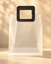 Frosted PVC gift bag with a stitched black square handle, front view
