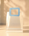 Frosted clear PVC gift bag with a stitched blue square handle, front view