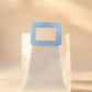 Clear PVC gift bag with blue square handle against a warm beige backdrop