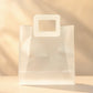 Clear PVC gift bag with off-white square handle, centered front view